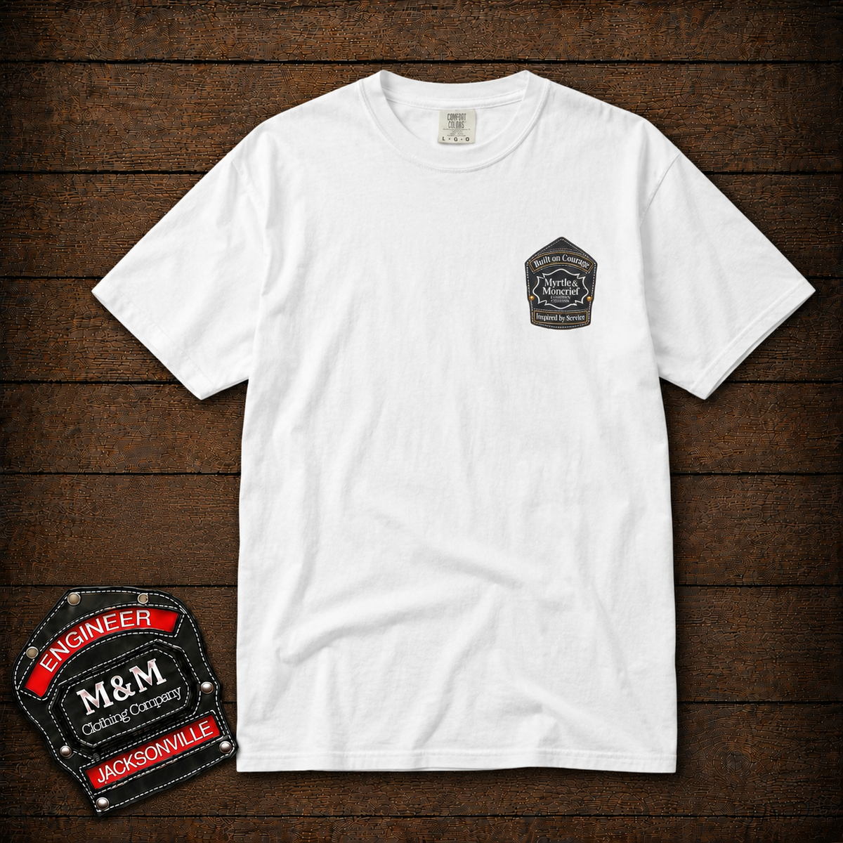 A white short-sleeve crewneck t-shirt with a small black and white Harley-Davidson logo patch printed on the left chest, displayed flat on a dark wood plank background. A larger version of the patch is shown in the bottom-left corner as an overlay.