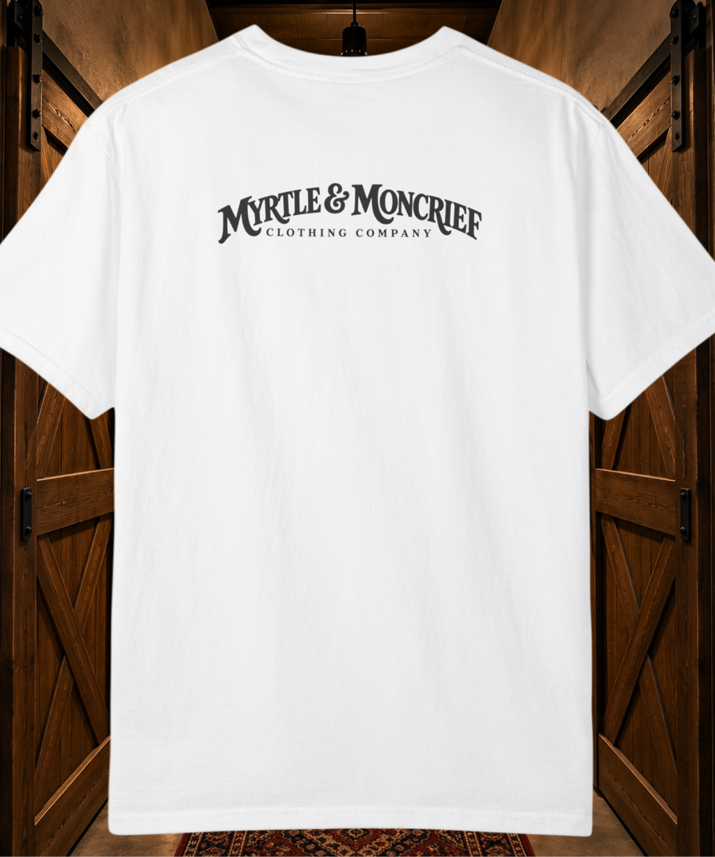 A white short-sleeve t-shirt with 'MYRLE & MONCRIEF CLOTHING COMPANY' printed in black arched text across the back, displayed against a rustic wooden barn door background.