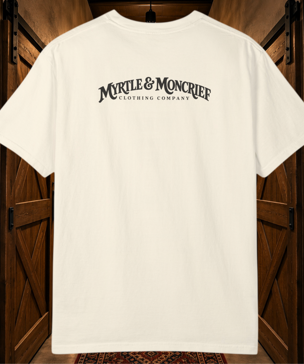 An off-white short-sleeve t-shirt with 'MYRLE & MONCRIEF CLOTHING COMPANY' printed in black across the back, displayed against a rustic dark wood barn door background.