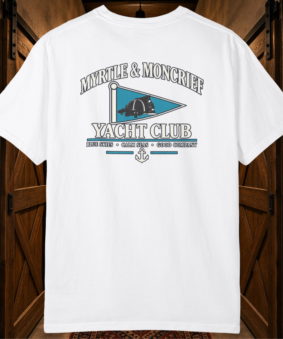 A white short-sleeve t-shirt with a vintage-style graphic on the back reading 'MYRTLE & MONCRIEF YACHT CLUB' with a teal flag design, displayed against a dark wood background.