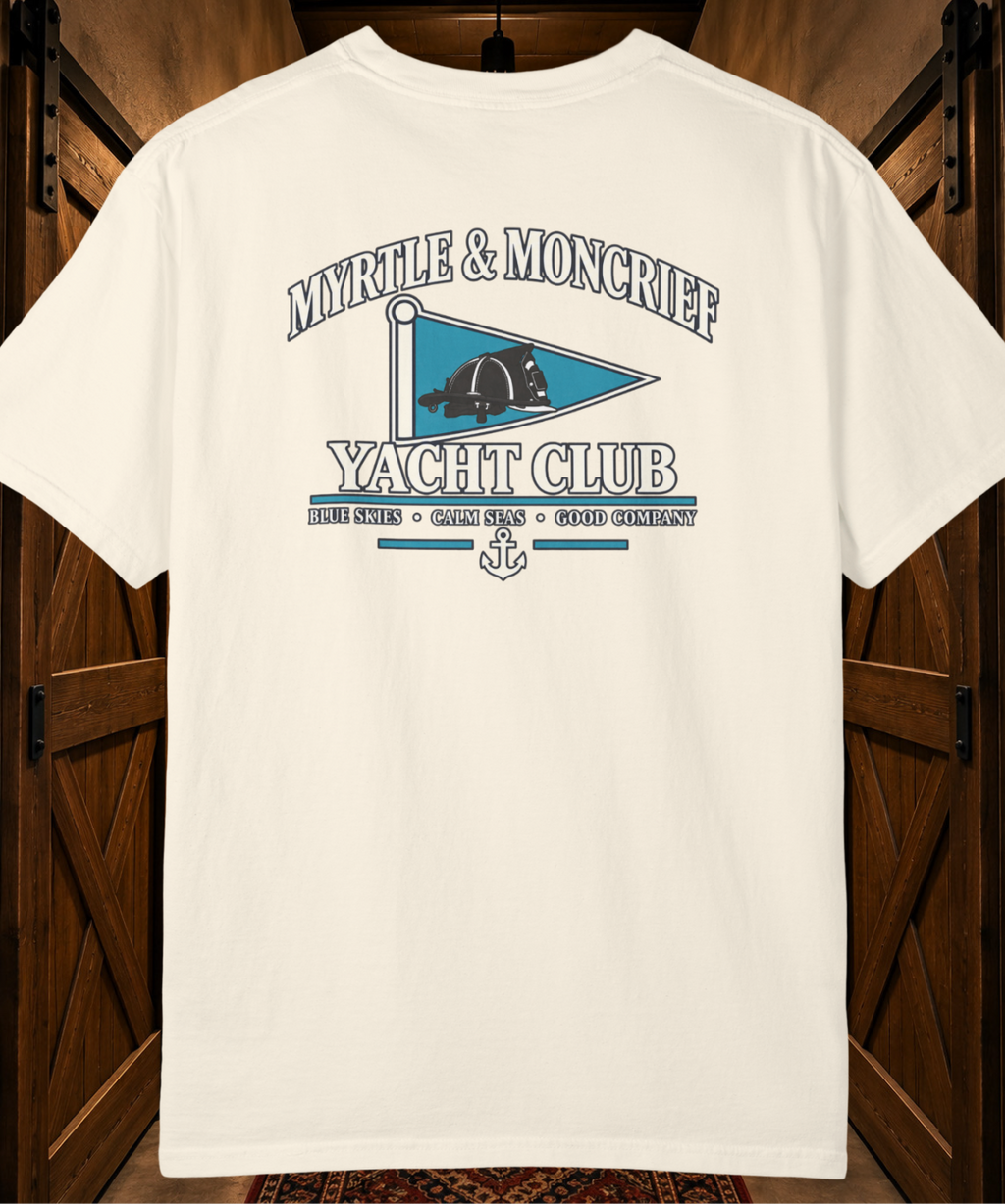 An off-white short-sleeve t-shirt with a vintage-style graphic on the back reading 'MYRTLE & MONCRIEF YACHT CLUB' with a teal flag design, displayed against a dark wood background.