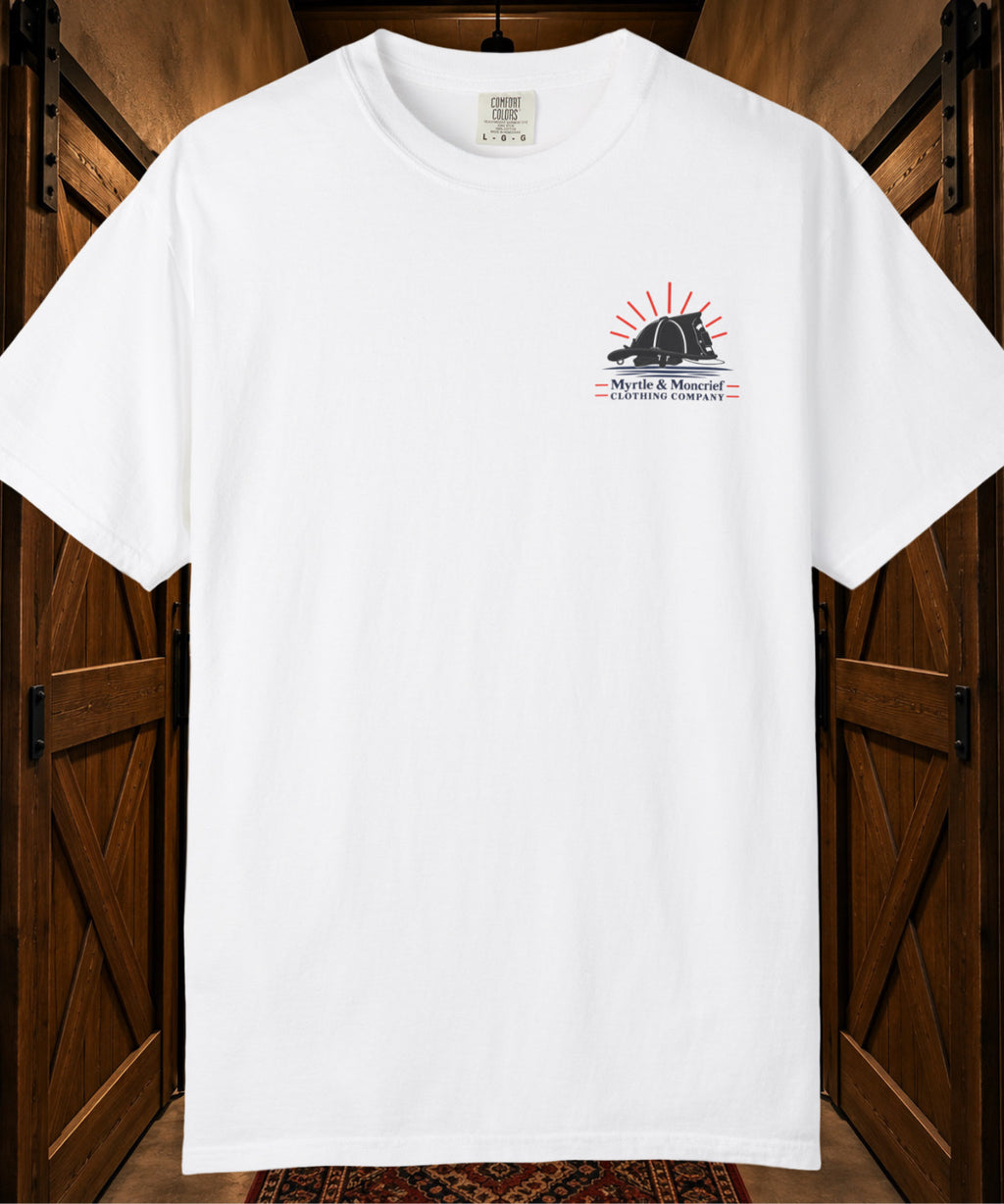 A white short-sleeve crewneck t-shirt hanging against a rustic wooden door background. The shirt features a small graphic on the left chest with a black fire helmet silhouette, red sun rays, and the text 'Myrtle & Moncrief CLOTHING COMPANY'.