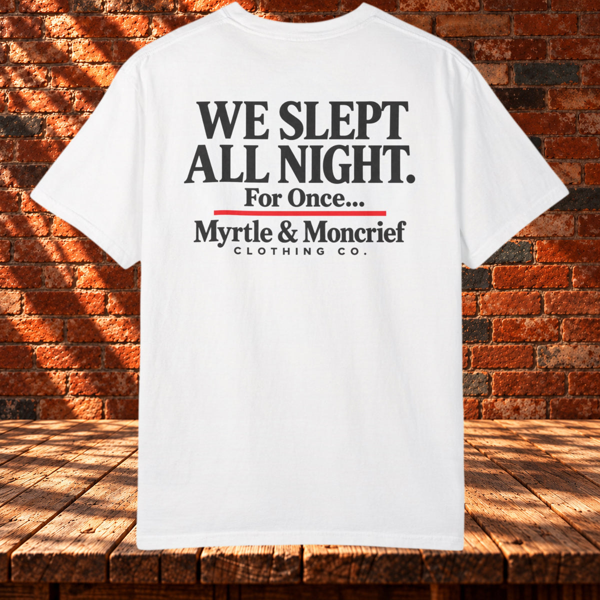 Back view: White T-shirt with “We Slept All Night. For Once...” in black, a red underline, and Myrtle & Moncrief Clothing Co. branding.